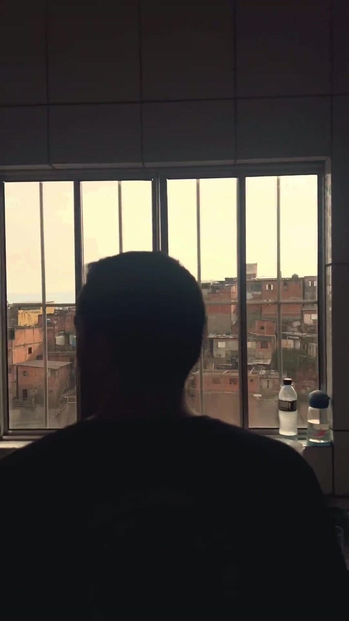 Integrante da equipe visto de costas, observando a comunidade pela janela gradeada
